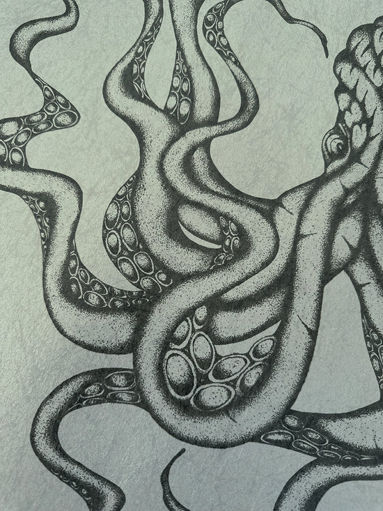 Close-up view of Kraken octopus tentacles in charcoal ink on parchment-style paper with coastal tones.