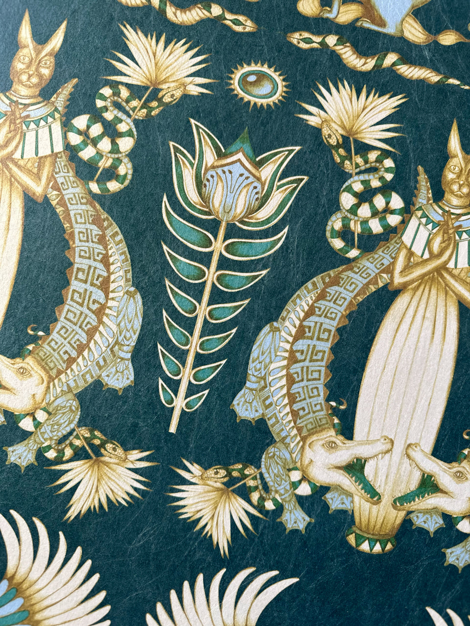 Verdigris coloured papyrus flowers and ivory-gold accents on illustrated Egyptian wallpaper.