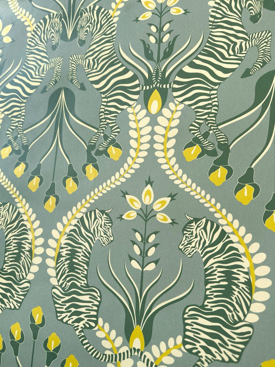 Close-up of Secret Garden Safari Grey wallpaper with tigers, zebras, and botanical pattern in ochre and eucalyptus tones.