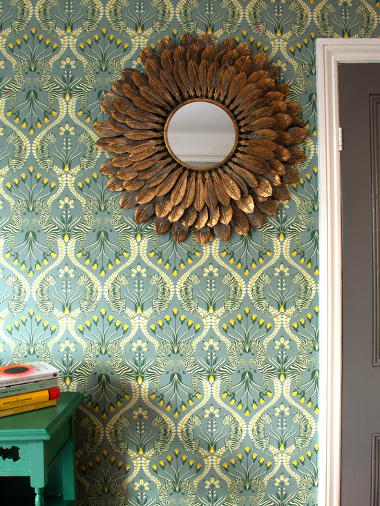 Living room styled with Secret Garden Safari Grey wallpaper featuring tigers, zebras and botanical print in ochre and eucalyptus.