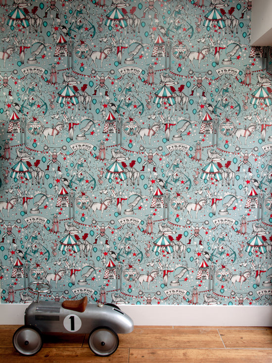 Maximalist full-wall circus repeat wallpaper in soft teal and cherry red tones.
