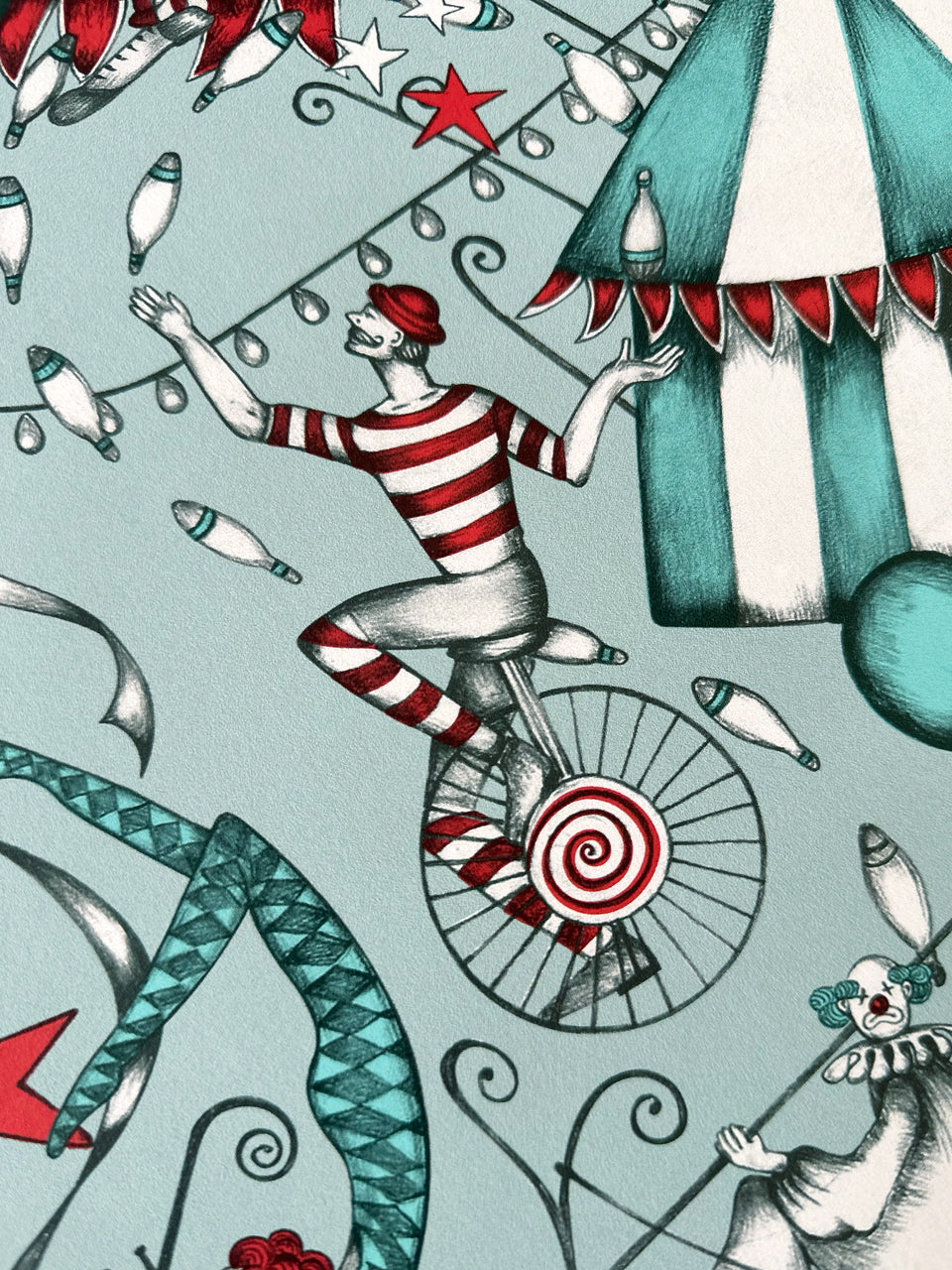 Carnival wallpaper with a clown and juggler on a unicycle in aqua and letterbox red.